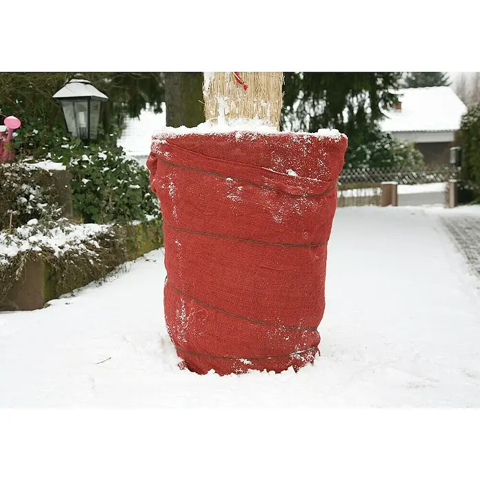 Floraworld Classic Jute-Gewebematte - Rot, 500 cm - Nahaufnahme eines mit einem roten Sack umwickelten Baumstamms, der mit Draht befestigt ist, im Winter mit Schnee bedeckt.