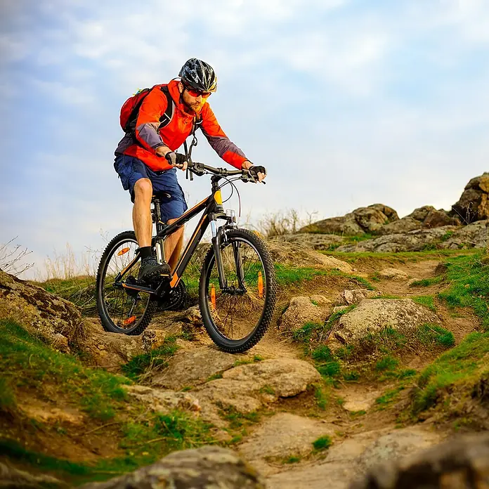 Luxshield Lackschutzfolie für Fahrräder - 5 -tlg. - Ein Mann fährt mit seinem Mountainbike auf einem steinigen Pfad. Das Bike hat eine auffällige schwarz-orange Farbgebung.