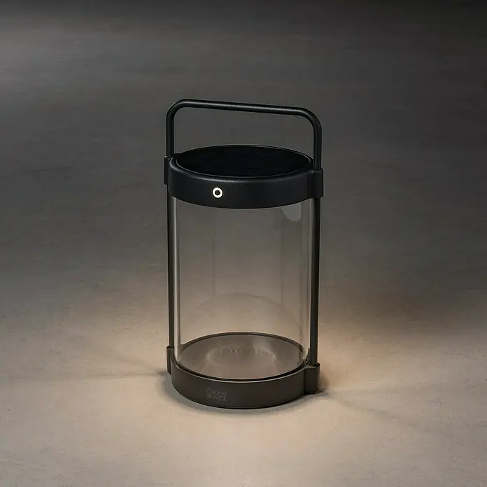 Konstsmide Außenlaterne Crotone - 17 x 15 x 30 cm, Schwarz - Eine moderne, zylindrische Tischleuchte in Schwarz mit einem klaren Glaszylinder, die ein warmes, stimmungsvolles Licht ausstrahlt.