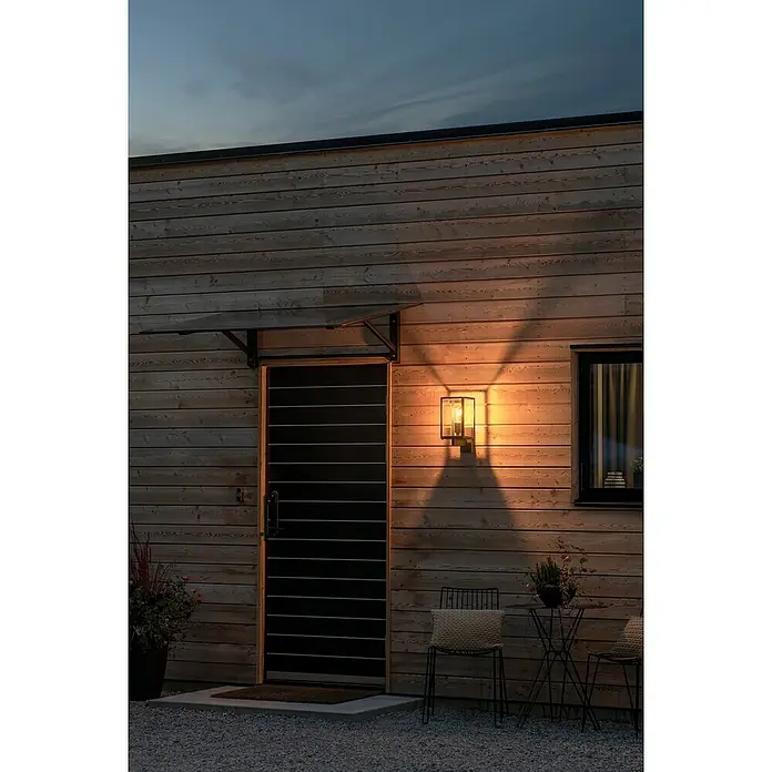 Konstsmide Außenwandleuchte Carpi - 21 x 16,5 x 33 cm, Schwarz, IP44 - Eine stilvolle Außenwandleuchte mit warmem Licht erhellt eine moderne Holzfassade und betont den Eingangsbereich.