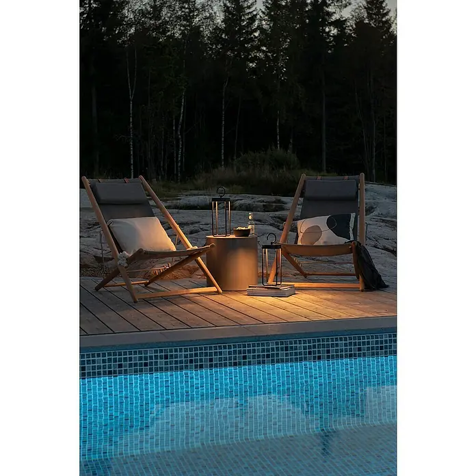 Konstsmide Außenlaterne Manorola - 15,5 x 15 x 39 cm, Schwarz - Nächtliche Entspannung am Pool mit zwei stilvollen Liegestühlen, beleuchtet von eleganten Laternen, die eine ruhige Atmosphäre schaffen.