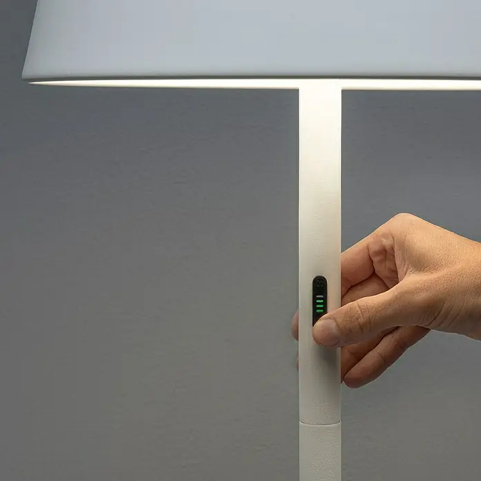 Konstsmide Außenleuchte Pomezia - Akkubetrieben, 10 W, RGBW, 35 x 35 x 150 cm, Mit Leuchtmittel, Weiß - Nahaufnahme einer Hand, die eine elegante, dimmbare LED-Stehleuchte mit minimalistischem Design bedient.