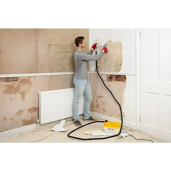 Wagner Dampf-Tapetenablöser Steam Force2.000 W, Behältervolumen: 4 l - Mann entfernt Tapeten mit einem gelben Wagner-Tapetenablöser. Das Gerät steht auf dem Boden. Renovierung eines Raumes.