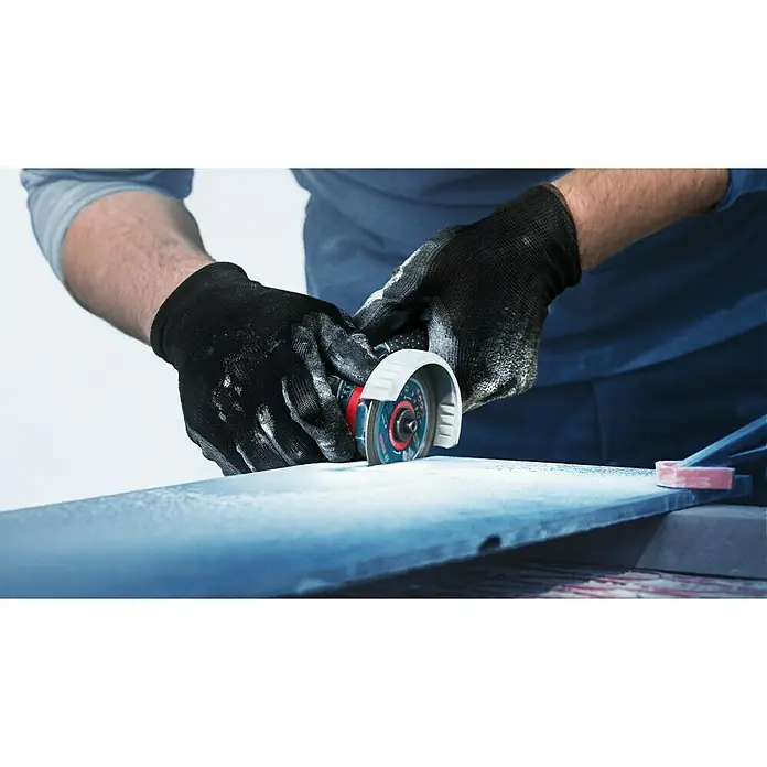 Bosch Expert Diamant-Trennscheibe Hard Ceramic - Geeignet für: Fliesen, Durchmesser Scheibe: 76 mm, 1 Stk. - Nahaufnahme einer Person mit schwarzen Handschuhen, die einen Winkelschleifer zum Schneiden eines Materials verwendet. Staubpartikel sind sichtbar.