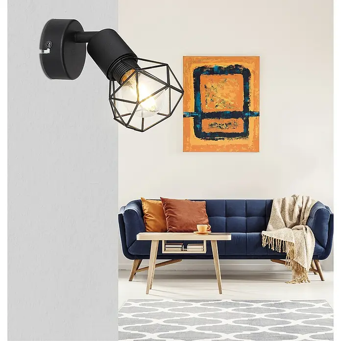 Globo Xara I Deckenstrahler - 40 W, B x H: 8 x 13,5 cm, Schwarz, E14, 1 Stk. - Diese Aufnahme zeigt eine schwarze Wandleuchte mit einem geometrischen Lampenschirm, die ein stilvolles Ambiente schafft. Sie hängt über einem blauen Sofa.