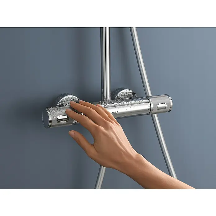 Grohe Vitalio Joy Duschsystem 260 - Mit Thermostatarmatur, Lochabstand: 100,5 cm, Anzahl Strahlarten: 3 Stk., Chrom - Eine Hand bedient eine Grohe Duscharmatur mit Thermostat vor einer grauen Wand.