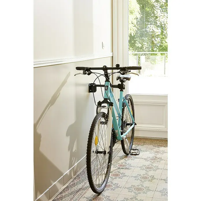 Mottez Fahrrad-Wandhaken - Stahl, Schwarz - Nahaufnahme eines an einer Wand montierten Fahrradträgers mit einem hellblauen Fahrrad, das sicher daran befestigt ist.