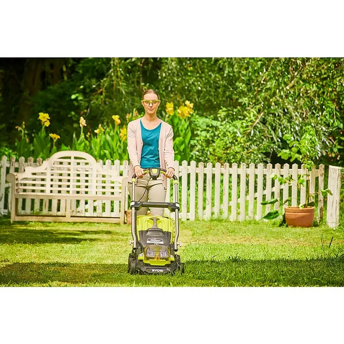 Ryobi ONE+ Akku-Rasenmäher RY18LMX40A-240 - 18 V, 2 Akkus, 4 Ah, Schnittbreite: 40 cm - Eine Frau im Garten, die einen gelben Ryobi-Rasenmäher bedient, umgeben von Grün und einem weißen Zaun.