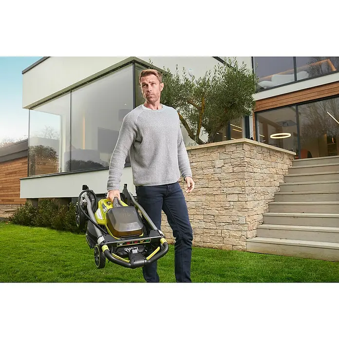 Ryobi ONE+ Akku-Rasenmäher RY18LMX40A-240 - 18 V, 2 Akkus, 4 Ah, Schnittbreite: 40 cm - Ein Mann trägt einen zusammengeklappten gelb-schwarzen Ryobi Rasenmäher vor einem modernen Haus mit Steintreppe.