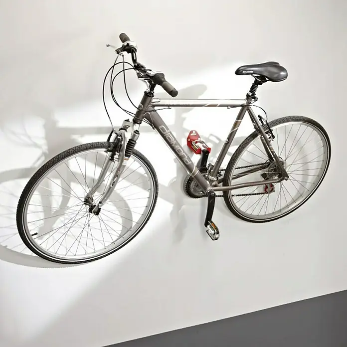 Mottez Gancho de pared para bicicletas B215V - Acero - Una bicicleta Diamond gris cuelga de una pared blanca, asegurada por un soporte rojo. La bicicleta es el producto principal.