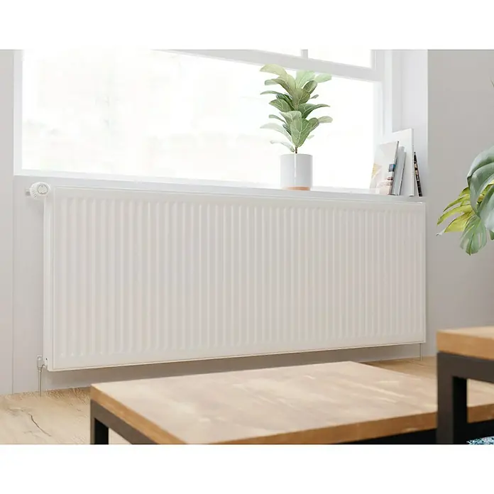 De'Longhi Kompaktheizkörper - B x H: 1.600 x 600 mm, Wärmeleistung bei Vorlauftemperatur von 75 °C (D: 50): 2.752 W, Typ Heizkörper: 22 - Ein weißer Heizkörper unter einem Fenster mit einer Pflanze darauf. Er sorgt für Wärme und Komfort in dem Raum mit hellem Holzfußboden.