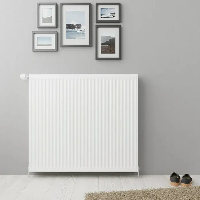 De'Longhi KompaktheizkörperB x H: 80 x 50 cm, Wärmeleistung bei Vorlauftemperatur von 75 °C (D: 50): 1.188 W, Typ Heizkörper: 22 - Nahaufnahme eines weißen Heizkörpers mit Rillen vor einer grauen Wand mit gerahmten Bildern für behagliche Wärme.