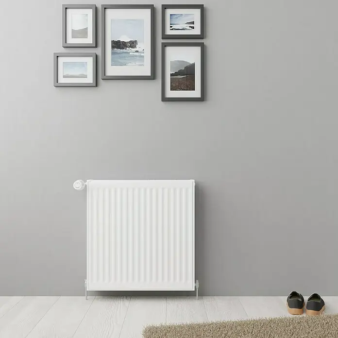 De'Longhi Kompaktheizkörper - B x H: 600 x 600 mm, Wärmeleistung bei Vorlauftemperatur von 75 °C (D: 50): 1.032 W, Typ Heizkörper: 22 - Eine Nahaufnahme eines weißen Heizkörpers vor einer grauen Wand mit gerahmten Bildern darüber. Perfekt für ein gemütliches Zuhause.