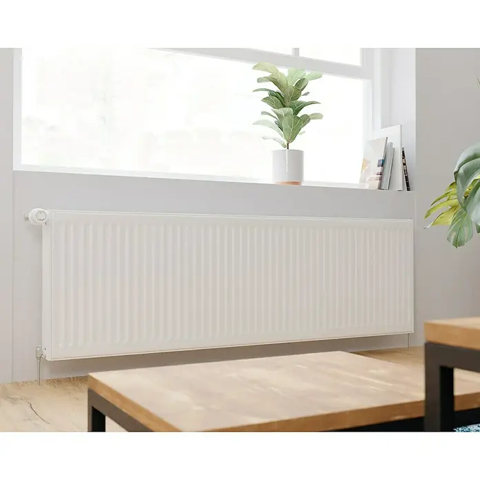 Kompaktheizkörper - B x H: 1.600 x 500 mm, Wärmeleistung bei Vorlauftemperatur von 75 °C (D: 50): 2.499 W, Typ Heizkörper: 22 - Dieses Bild zeigt einen weißen Heizkörper unter einem Fenster, mit einer Zimmerpflanze oben. Das Design ist schlicht und modern.