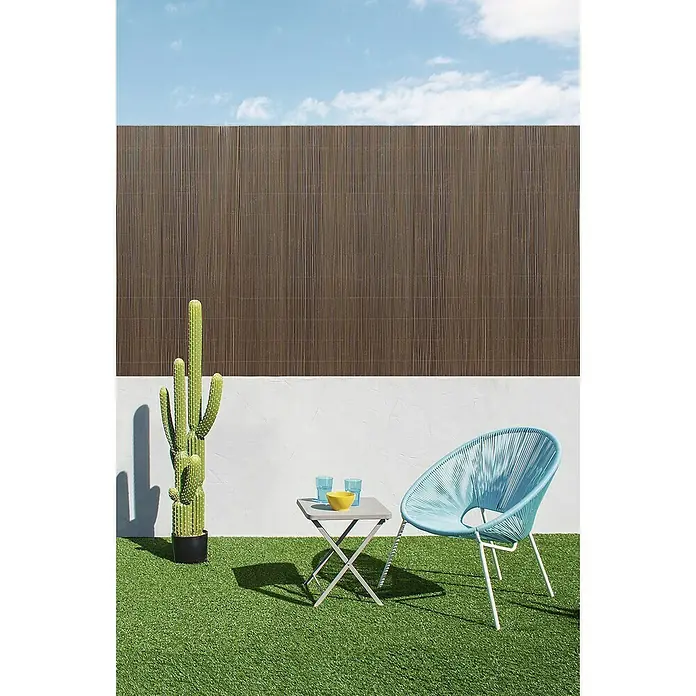 Nortene Sichtschutzmatte LOP - L x H: 300 x 90 cm - Outdoor-Szene mit einem modernen blauen Sessel, einem kleinen Tisch mit farbigen Gläsern und einer Kaktuspflanze vor einem stilvollen Holzzaun.