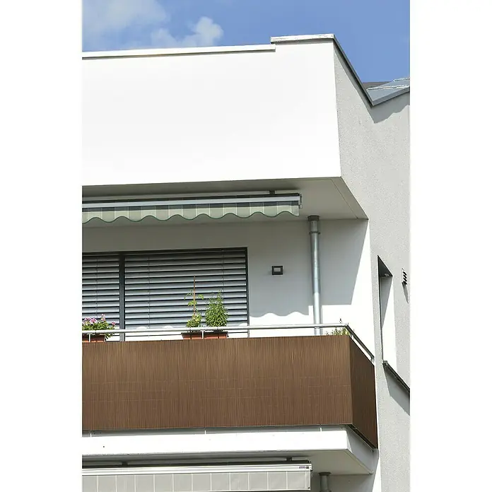 Nortene Sichtschutzmatte Wood - L x H: 3 x 1,8 m, Bambus Optik - Nahaufnahme eines Balkons mit Sichtschutz, Pflanzen und einer Markise vor einem weißen Gebäude unter blauem Himmel.
