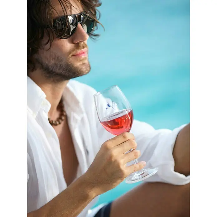 Marine Business Welcome on Board Copa de vino - 6 ud., Plástico, Transparente - Hombre con gafas de sol que sostiene una copa de vino rosado frente a un fondo azul.