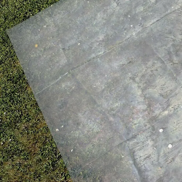 Gre Piscina de acero desmontable Mauritius - L x An x Al: 610 x 375 x 132 cm, Marrón claro, 23.281 l - Una lámina de plástico transparente rectangular sobre una pradera verde, revelando parcialmente el césped debajo.