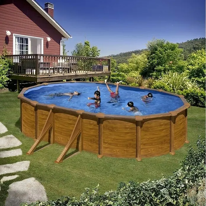 Gre Piscina de acero desmontable Mauritius - L x An x Al: 610 x 375 x 132 cm, Marrón claro, 23.281 l - La imagen muestra una piscina ovalada de madera elevada con niños jugando en el agua, rodeada de un jardín verde y una casa.
