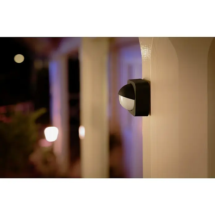 Philips Hue Bewegungsmelder - Reichweite Sensor: 12 m, Schwarz, L x B x H: 7,5 x 17,6 x 16,5 cm - Außenaufnahme eines schwarzen Philips Hue Bewegungsmelders an einer beigen Säule bei Nacht.