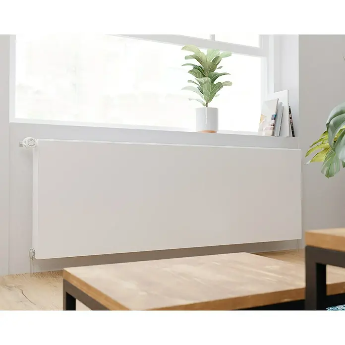 E.C.A. Planheizkörper - B x H: 1.600 x 550 mm, 2.494 W, 22 - Nahaufnahme eines weißen Heizkörpers unter einem Fenster mit Topfpflanze und Büchern für gemütliche Wärme und stilvolles Ambiente.