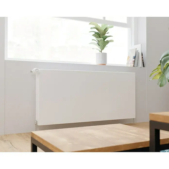 E.C.A. Planheizkörper - B x H: 1.200 x 550 mm, 1.871 W, 22 - Zimmeransicht mit einem weißen Heizkörper unter einem Fenster, auf dem eine Zimmerpflanze steht. Der Heizkörper ist modern und unauffällig.