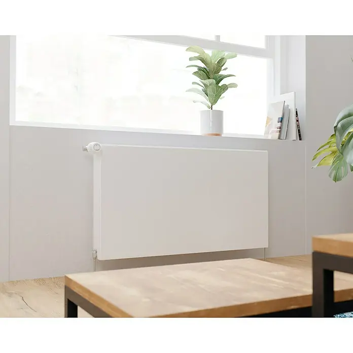 E.C.A. Planheizkörper - B x H: 1.000 x 550 mm, 1.559 W, 22 - Ein weißer Heizkörper unter einem Fenster mit Zimmerpflanzen darauf. Der Heizkörper fügt sich nahtlos in die helle Wand ein.