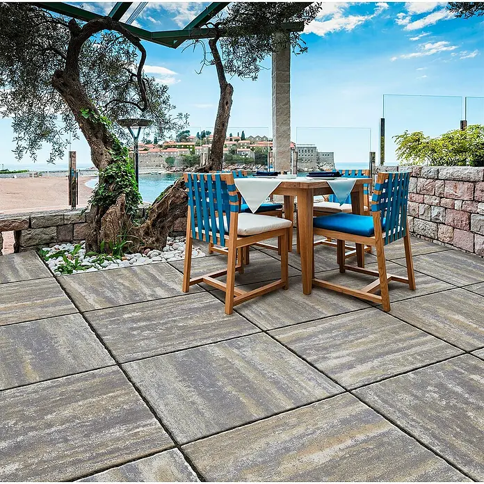 Terrassenplatte Ellenica - 48 x 48 x 3,2 cm, Muschelkalk, Beton - Elegantes Terrassenbild mit hellgrauen Pflastersteinen, die eine stilvolle Außenfläche schaffen. Ideal für Restaurants und Gärten.
