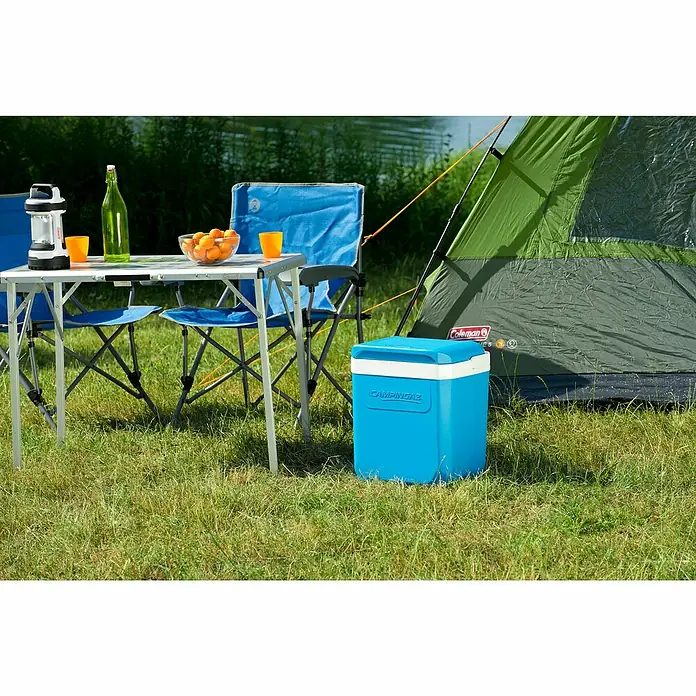 Campingaz Nevera de camping Icetime Plus - 26 l, 22,7 x 31,2 x 33 cm - Escena de camping con nevera azul Campingaz, mesa, sillas y tienda sobre una verde pradera cerca del agua.