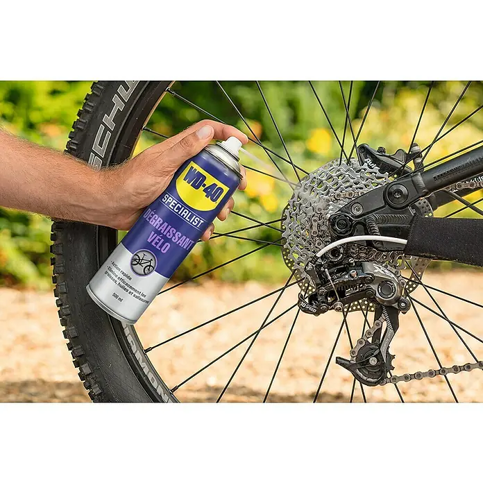 WD-40 Bike Lubricante - 500 ml - Un hombre rocía desengrasante para bicicletas WD-40 en el piñón de una bicicleta para limpiarlo.