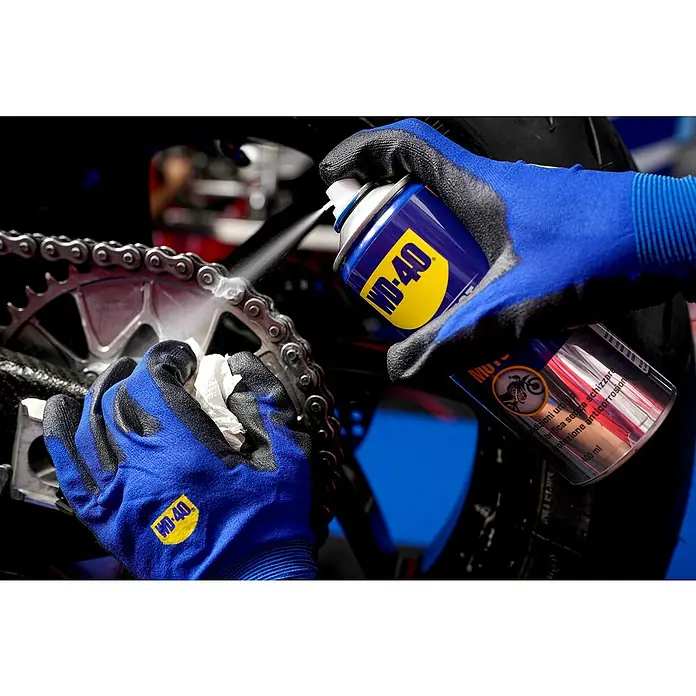 WD-40 Specialist Motorbike Grasa para cadena - 400 ml - La imagen muestra WD-40 siendo usado para limpiar una cadena de motocicleta, con guantes azules.
