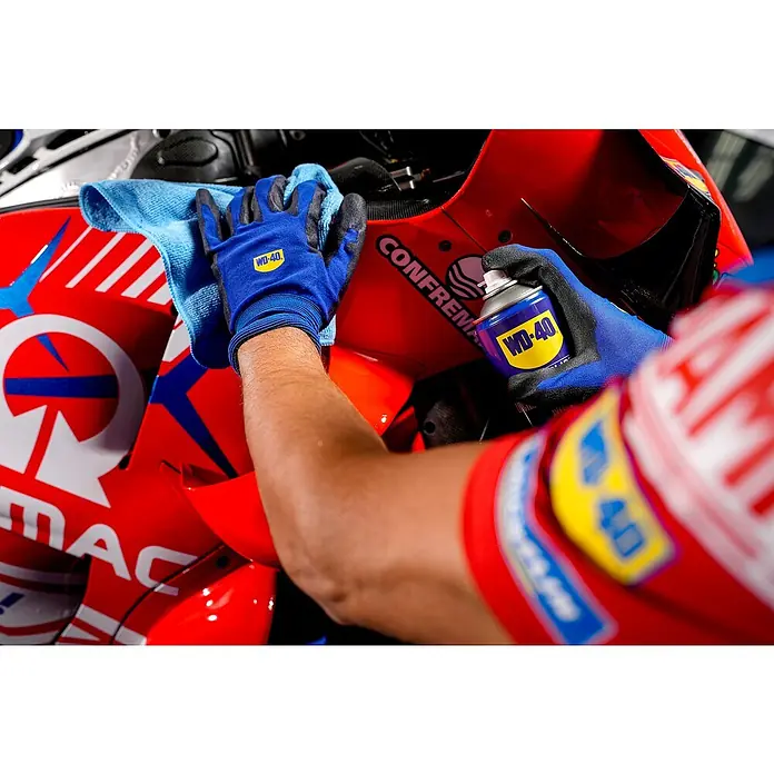 WD-40 Limpiador abrillantador de silicona - 400 ml - Un hombre limpia una motocicleta con WD-40 y un paño azul para mantenimiento y protección. El logotipo de WD-40 es claramente visible.