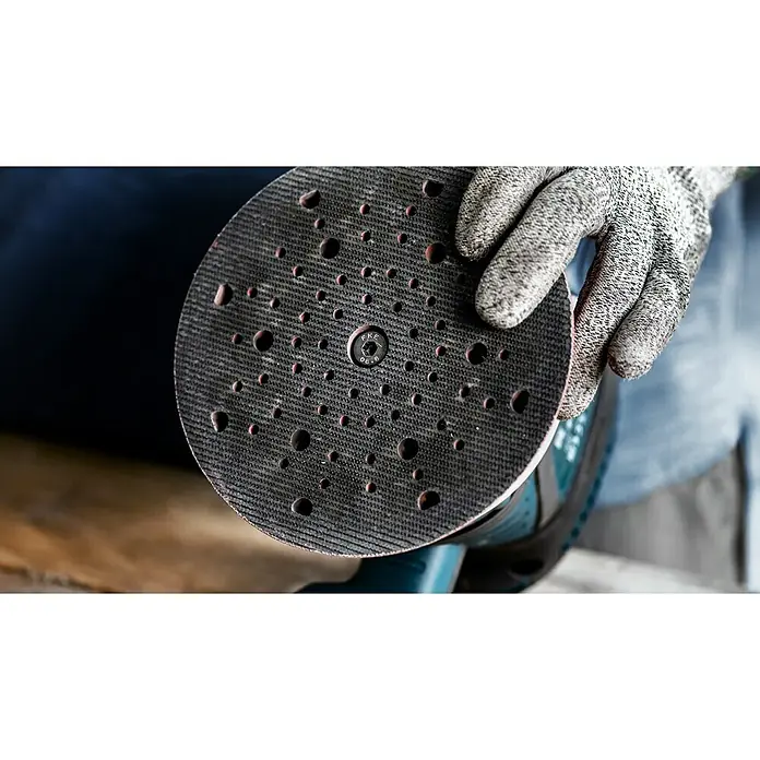 Bosch Expert Stützteller Multihole150 mm, Gelocht, Passend für: Exzenterschleifer - Nahaufnahme eines Schleifpads mit Löchern, das von einer behandschuhten Hand gehalten wird. Ein Werkzeug für präzises Schleifen in der Werkstatt.