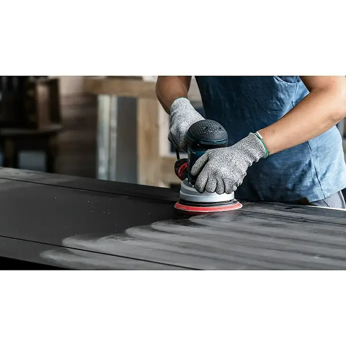 Bosch Expert Stützteller Multihole - 125 mm, Gelocht, Passend für: Exzenterschleifer - Mann schleift mit einer Schleifmaschine eine schwarze Oberfläche. Der Bosch-Exzenterschleifer sorgt für ein optimales Schleifergebnis.