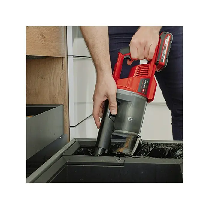 Einhell PXC 18V Aspirador de batería TE-SV 18 Li-Solo - 18 V, Sin batería, Volumen de recipiente: 0,6 l - Una persona vacía una aspiradora inalámbrica Einhell roja en un cubo de basura con una bolsa negra.