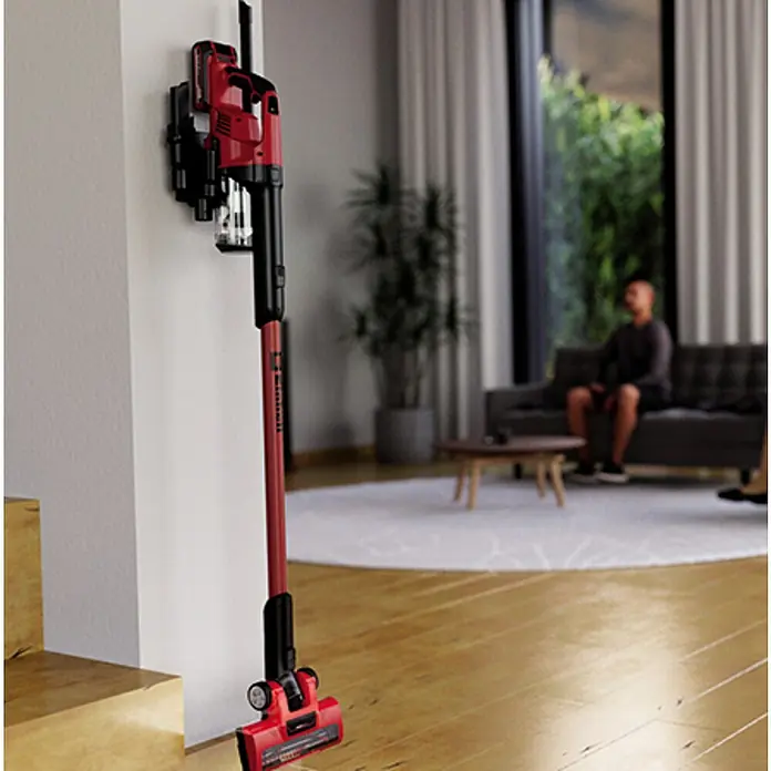 Einhell PXC 18V Aspirador de batería TE-SV 18 Li-Solo - 18 V, Sin batería, Volumen de recipiente: 0,6 l - Aspiradora inalámbrica roja con soporte de pared en una sala de estar moderna. Almacenamiento cómodo y carga rápida.