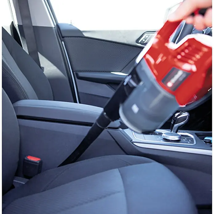 Einhell PXC 18V Aspirador de batería TE-SV 18 Li-Solo - 18 V, Sin batería, Volumen de recipiente: 0,6 l - Se está utilizando una aspiradora de mano roja para limpiar el interior de un coche, centrándose en la limpieza de la zona del asiento.