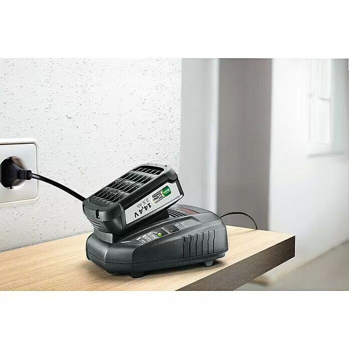 Bosch Power for All 18V Cargador de baterías AL 1830 CV - 18 V, 2,5 Ah - Una batería negra Bosch 14,4V 2,5 Ah Li-ION+ está insertada en un cargador negro, enchufada a una toma de corriente blanca, con luz verde de carga.
