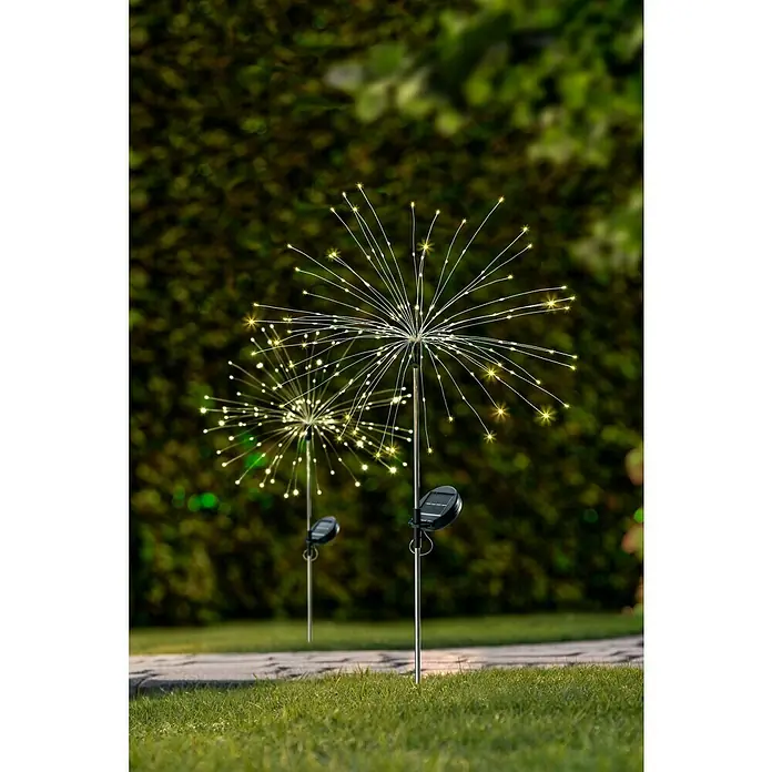 BAUHAUS Solarleuchte FeuerwerkHöhe: 90 cm, IP44, Lichtfarbe: Warmweiß - Zwei Solar-Gartenleuchten in Form von Feuerwerkskörpern, die im Garten aufgestellt sind und ein warmes, gelbes Licht ausstrahlen.