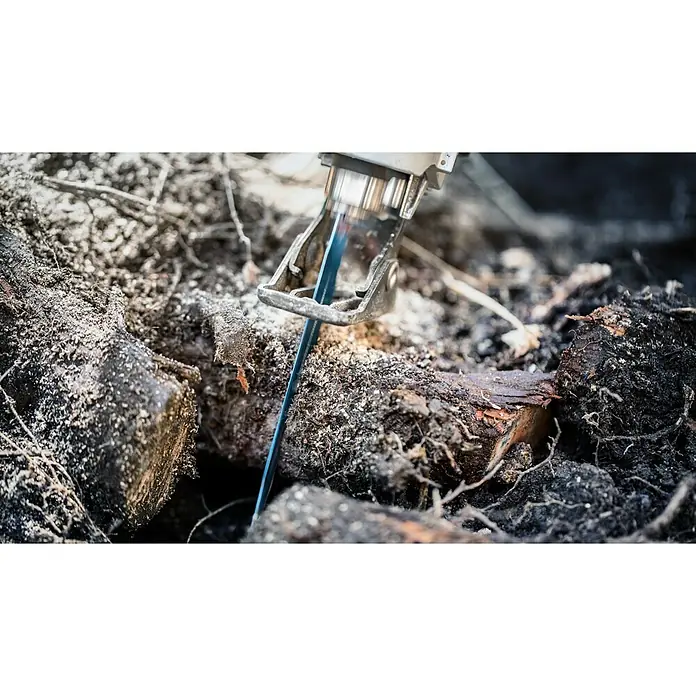 Bosch Expert Säbelsägeblatt Tough Wood S 1142 KHM - Länge: 225 mm - Nahaufnahme einer Metallsäge, die durch ein Stück Holz schneidet, umgeben von Sägemehl und Erde, was Präzision und Handwerkskunst hervorhebt.