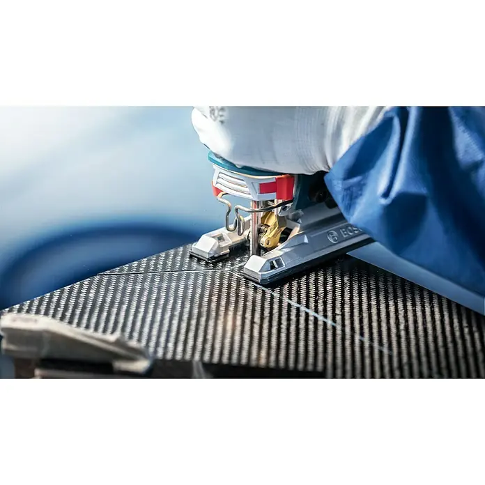 Bosch Expert Stichsägeblatt Carbon Fiber Clean T108 BHM - Länge: 92 mm, T-Schaft - Detailaufnahme einer Stichsäge beim Schneiden eines Werkstücks mit Kohlefasermuster. Die Hand des Bedieners ist durch einen Handschuh geschützt.