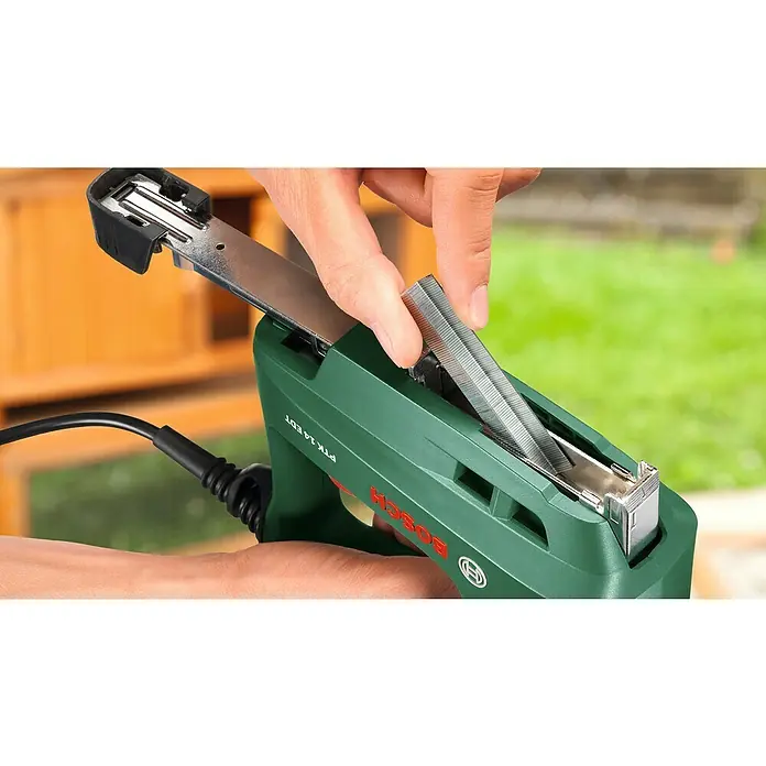Bosch Elektrotacker PTK 14 EDT - Klammertiefe: 6 mm - 14 mm, 30 Impulse/min - Nahaufnahme einer Person, die eine Reihe von Heftklammern in einen grünen Bosch PTK 14 EDT Elektrotacker einlegt.