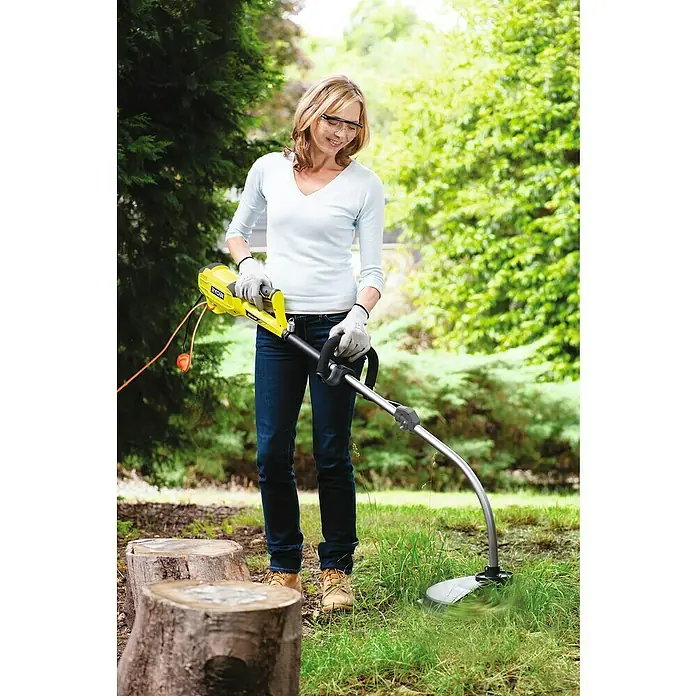 Ryobi Elektro-Rasentrimmer RLT1238I - 1.200 W - Eine Frau benutzt einen RYOBI Rasentrimmer im Garten, um das Gras zu schneiden. Sie trägt Schutzkleidung für die Gartenarbeit.