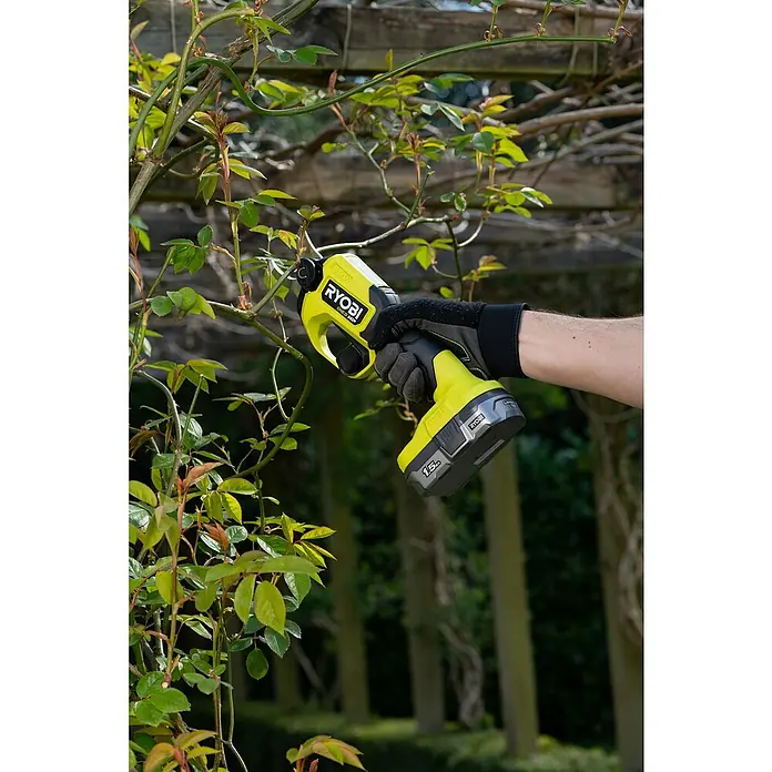Ryobi ONE+HP Akku-Gartenschere RY18SCXA-0 - 18 V, Li-Ionen, Ohne Akku, Max. Aststärke: 28 mm - Nahaufnahme einer Ryobi Astschere beim Beschneiden eines buschigen Strauchs im Garten, gehalten von einer Hand mit Handschuh.
