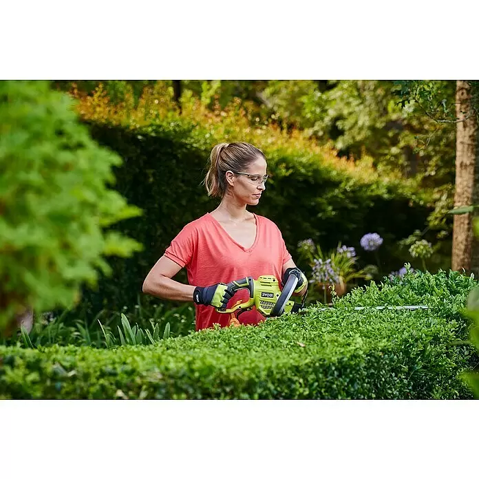 Ryobi Elektro-Heckenschere RHT4550 - 450 W, Schnittlänge: 50 cm, Max. Aststärke: 20 mm - Eine Frau trimmt eine grüne Hecke mit einer grün-schwarzen Ryobi Heckenschere.