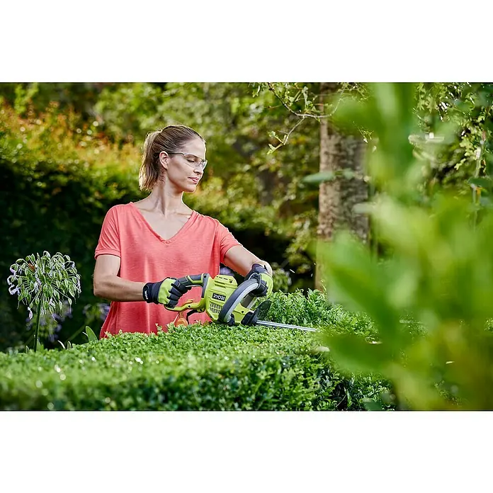 Ryobi Cortasetos eléctrico RHT4550 - 450 W, Longitud de corte: 50 cm, Grosor de rama máx.: 20 mm - Una mujer poda un seto con un cortasetos inalámbrico verde RYOBI. El cortasetos es inalámbrico, lo que permite un trabajo flexible en el jardín.