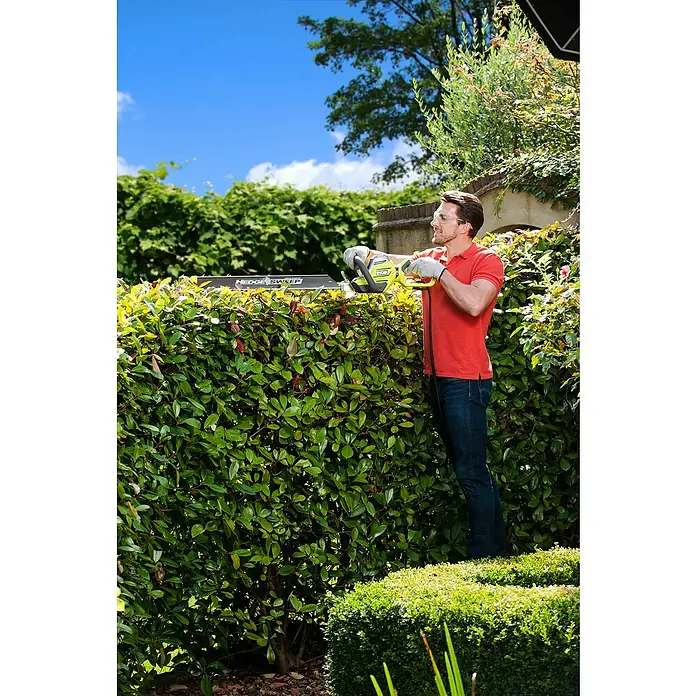 Ryobi Elektro-Heckenschere RHT6760RL - 650 W, Schnittlänge: 60 cm, Max. Aststärke: 30 mm - Mann trimmt Hecke mit Ryobi Heckenschere, mit Fokus auf Komfort und Leistung für mühelose Gartenarbeit.