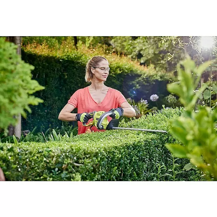 Ryobi Elektro-Heckenschere RHT4550 - 450 W, Schnittlänge: 50 cm, Max. Aststärke: 20 mm - Frau mit Schutzbrille und Handschuhen trimmt mit einer grün-schwarzen Heckenschere eine Hecke.