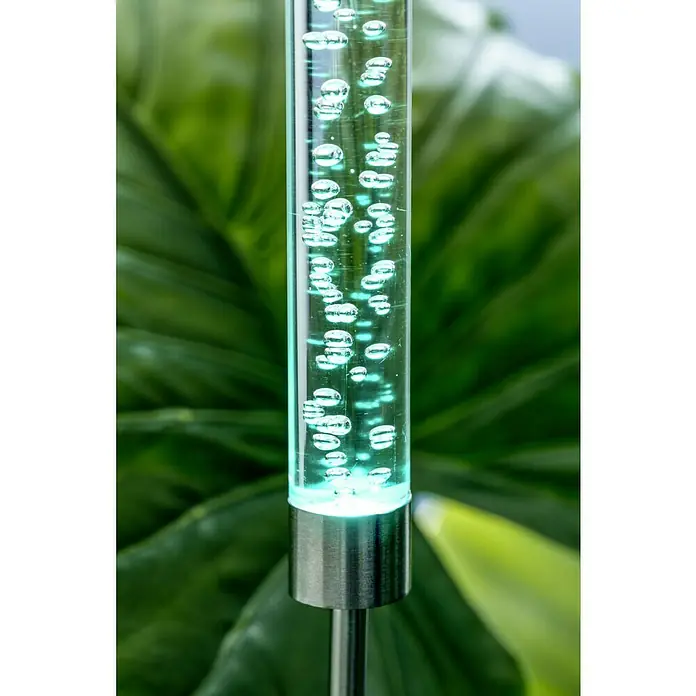 BAUHAUS Lámpara decorativa solar Bubble - 0,06 W, Transparente, IP44 - Primer plano de una lámpara solar con burbujas de aire y base de acero inoxidable sobre fondo verde.