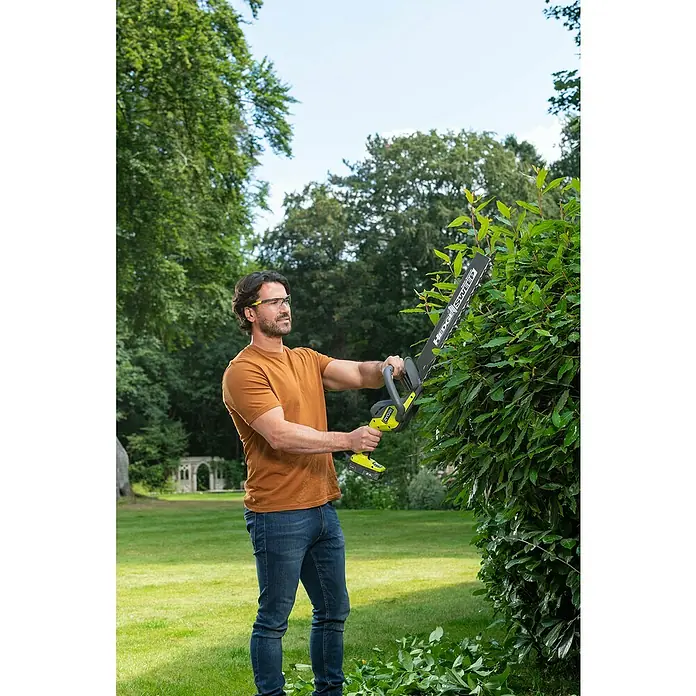 Ryobi ONE+ Akku-Heckenschere RY18HT45A-0 - 18 V, Li-Ionen, Ohne Akku - Ein Mann schneidet mit einer Ryobi Heckenschere eine Hecke im Garten. Die Heckenschere ist kabellos und hat einen langen Schaft für mehr Reichweite.
